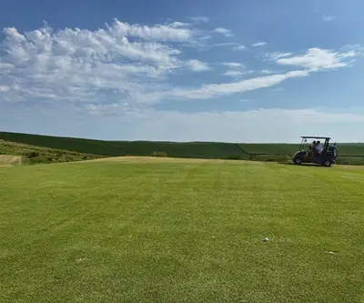 Golf cart beside a wide open fairway with rolling farmland and blue sky at Landmand Golf Club in Homer, Nebraska