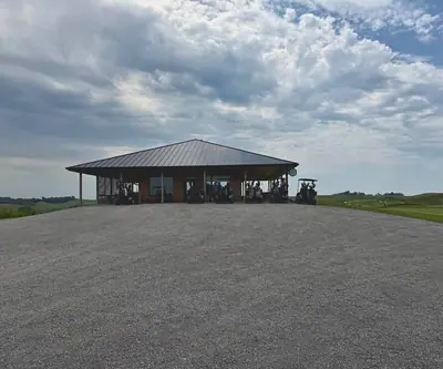 Metal-roofed pavilion with golf carts parked on a gravel lot under cloudy skies at Landmand Golf Club in Homer, Nebraska