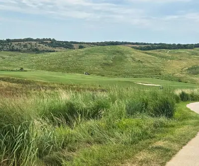 Rolling prairie hills and native grass beside a cart path and bunkered fairway at Landmand Golf Club in Homer, Nebraska