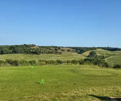 Tee box with green markers facing rolling tree-covered hills at Landmand Golf Club in Homer, Nebraska