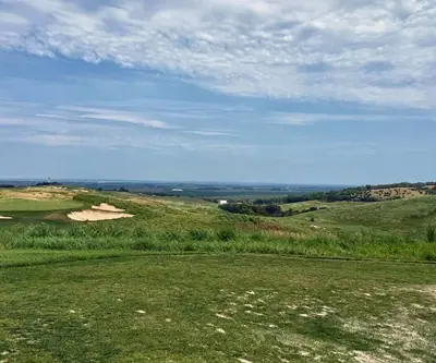 Tee view over native grass to a green with bunkers and distant farmland at Landmand Golf Club in Homer, Nebraska