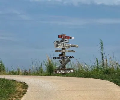 Wooden directional signpost with hand-painted arrows beside a cart path at Landmand Golf Club in Homer, Nebraska