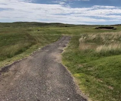 Worn gravel cart path through native grasses toward rolling Sandhills at Pelican Beach Golf Course in Hyannis, Nebraska