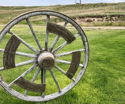 Wagon wheel hole 1 sign reading par 4, 369 yards, with sponsor plaques at Pelican Beach Golf Course in Hyannis, Nebraska