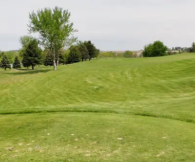 Teed-up ball above a fairway that dips into a valley and climbs past evergreens at Club 91 Golf Course in Leigh, Nebraska