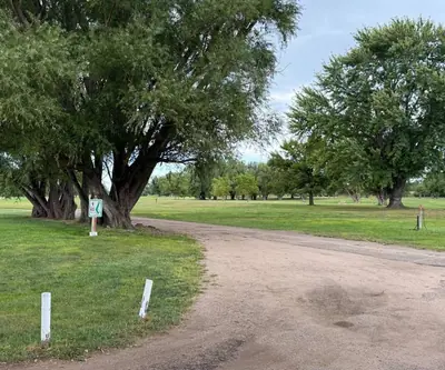 Dirt cart path curving past large willow trees and a small sign at Loup City Golf Club in Loup City, Nebraska
