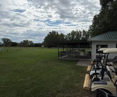 Clubhouse with a green metal roof and covered pavilion beside parked golf carts at Loup City Golf Club in Loup City, Nebraska