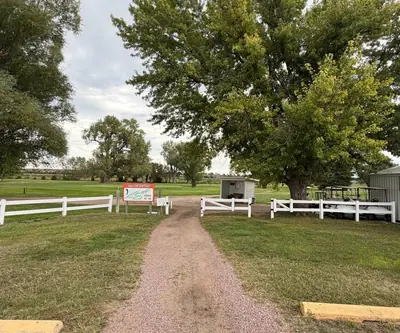 Gravel path between white fences to the course sign and parked golf carts at Loup City Golf Club in Loup City, Nebraska