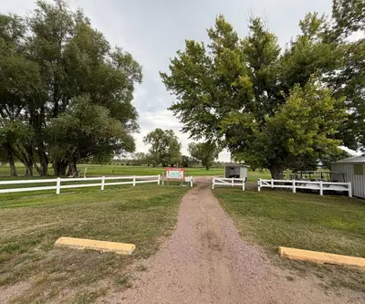 Gravel entry path past a white fence, course map sign and cart shed at Loup City Golf Club in Loup City, Nebraska