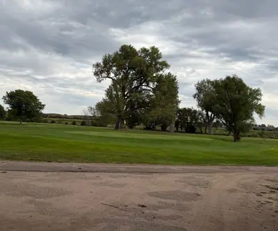 Green with yellow flag beneath large cottonwoods on a cloudy day at Loup City Golf Club in Loup City, Nebraska