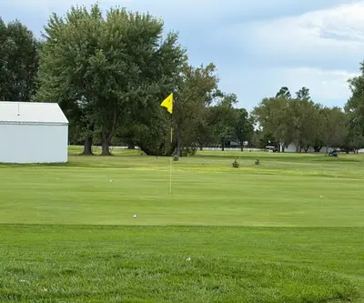Putting green with a yellow flag and golf balls beside a white shed at Loup City Golf Club in Loup City, Nebraska
