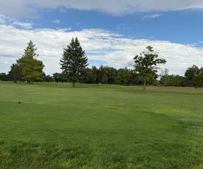 Red tee marker looking out over an open fairway lined with evergreens at Loup City Golf Club in Loup City, Nebraska
