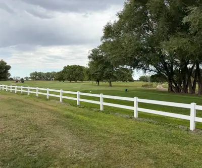 White rail fence along a tree-shaded fairway under cloudy skies at Loup City Golf Club in Loup City, Nebraska