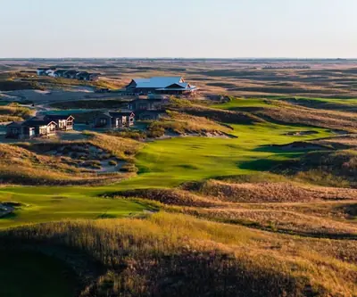 Aerial view of the clubhouse and cottages above a fairway in rolling prairie at GrayBull Golf Club in Maxwell, Nebraska