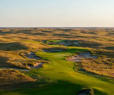 Aerial view of a fairway winding past sandy bunkers and golden prairie grass at GrayBull Golf Club in Maxwell, Nebraska