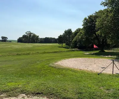 Sand green with red flag and drag beside tall shade trees at Shell Creek Valley Golf Course in Newman Grove, Nebraska