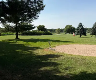 Sand green with a red flag and drag rake beside pine trees at Shell Creek Valley Golf Course in Newman Grove, Nebraska
