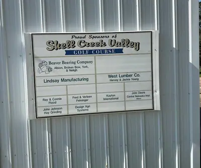 Sponsor board listing local businesses on a white metal building at Shell Creek Valley Golf Course in Newman Grove, Nebraska