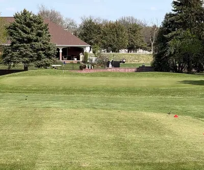 Green in front of a brick building with a covered patio and evergreens at O'Neill Golf Club in O'Neill, Nebraska