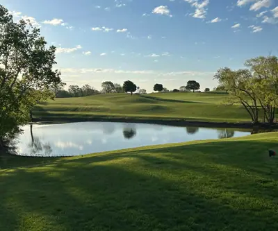 Pond reflecting trees below rolling fairways under a blue sky at Lake Ridge Golf Course in Plattsmouth, Nebraska