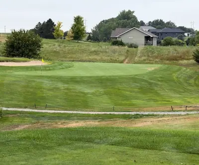 Green with yellow flag and bunker below grassy slopes and homes at The Greens At Prairie Hills in Pleasanton, Nebraska