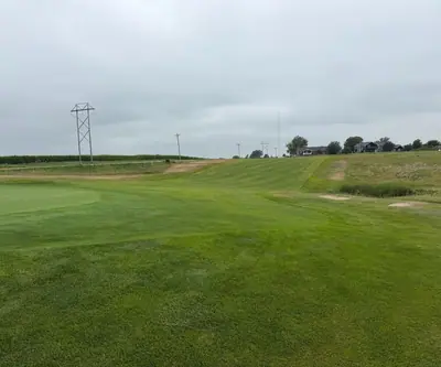 Green and uphill fairway beside a cornfield and power lines at The Greens At Prairie Hills in Pleasanton, Nebraska