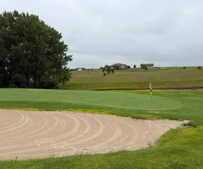 Raked sand bunker guarding a green with a yellow flag at The Greens At Prairie Hills in Pleasanton, Nebraska