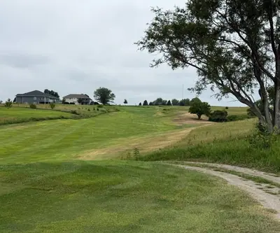 Striped fairway climbing toward hillside homes beside a gravel path at The Greens At Prairie Hills in Pleasanton, Nebraska