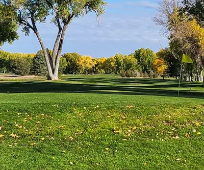 Fallen leaves on the green by a yellow flag with golden fall trees behind at Riverview Golf Course in Scottsbluff, Nebraska