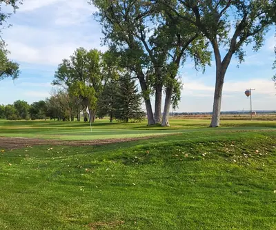 Green framed by tall cottonwoods with a hot air balloon in the sky at Riverview Golf Course in Scottsbluff, Nebraska