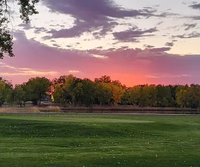 Pink sunset over a green with a yellow flag and autumn trees at Riverview Golf Course in Scottsbluff, Nebraska