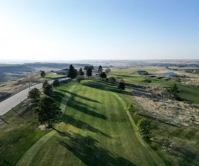 Drone view down a striped, pine-lined fairway above open plains at Hillside Golf Course in Sidney, Nebraska