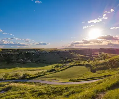 Sun setting over rugged bluffs above a mowed fairway and winding cart path at Hillside Golf Course in Sidney, Nebraska