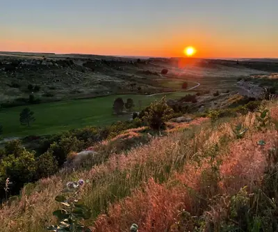 Sunset over a prairie canyon and winding fairway framed by wild grasses at Hillside Golf Course in Sidney, Nebraska