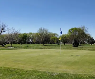 Putting green with a blue flag and golf carts among spring trees at St. Paul Country Club in St. Paul, Nebraska