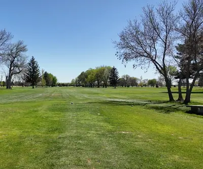Tee box with ball washer and bench facing an open tree-lined fairway at St. Paul Country Club in St. Paul, Nebraska