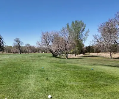 Tee view down a fairway lined with bare spring trees under a blue sky at St. Paul Country Club in St. Paul, Nebraska
