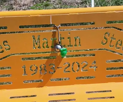 Yellow memorial bench with cut-out lettering and 1983-2024 dates at St. Paul Country Club in St. Paul, Nebraska